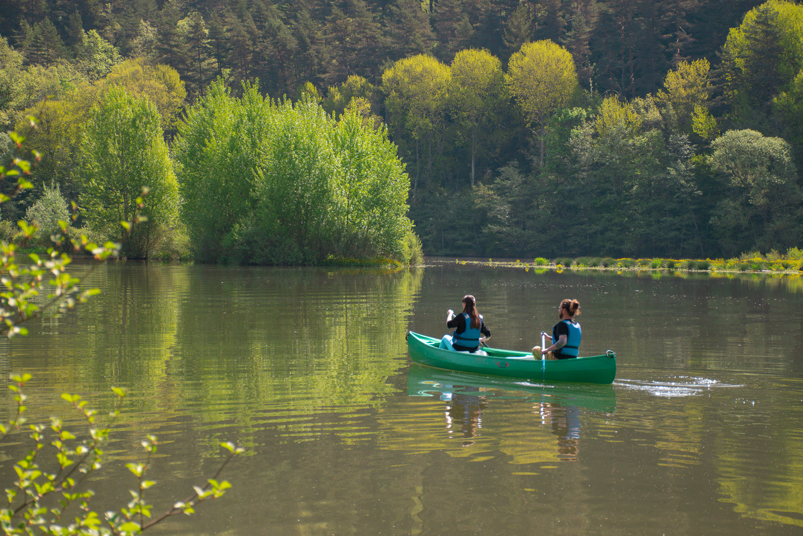Sur la rivière du Lot, un homme et une femme font du canoë. En fond de photo, il y a une forêt verdoyante. Ce moment de sport de pleine aire inspire le calme et de détente.